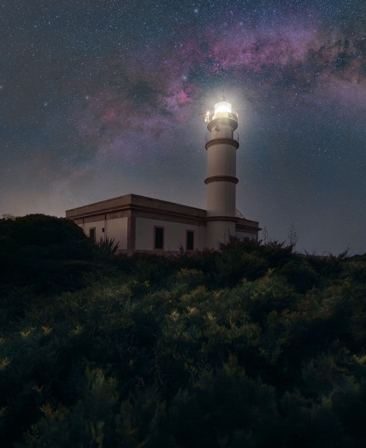 A lighthouse shining under a star filled sky